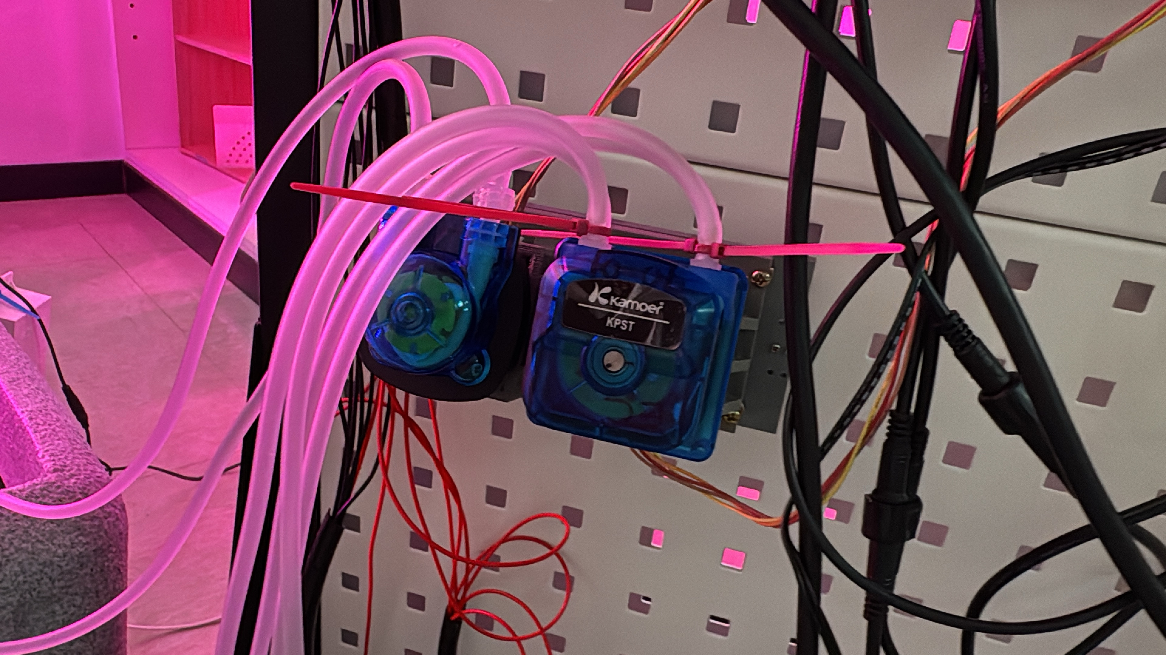 Two peristaltic pumps under a purple light emanating from an indoor farm.